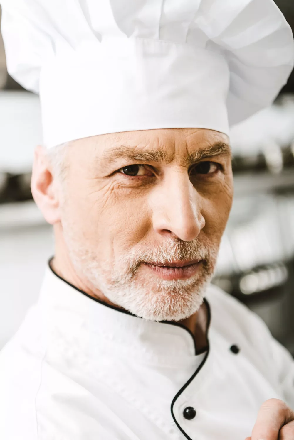 Gros plan du chef Maxime Laurent en toque blanche, regard sérieux, incarnant authenticité et expertise culinaire.